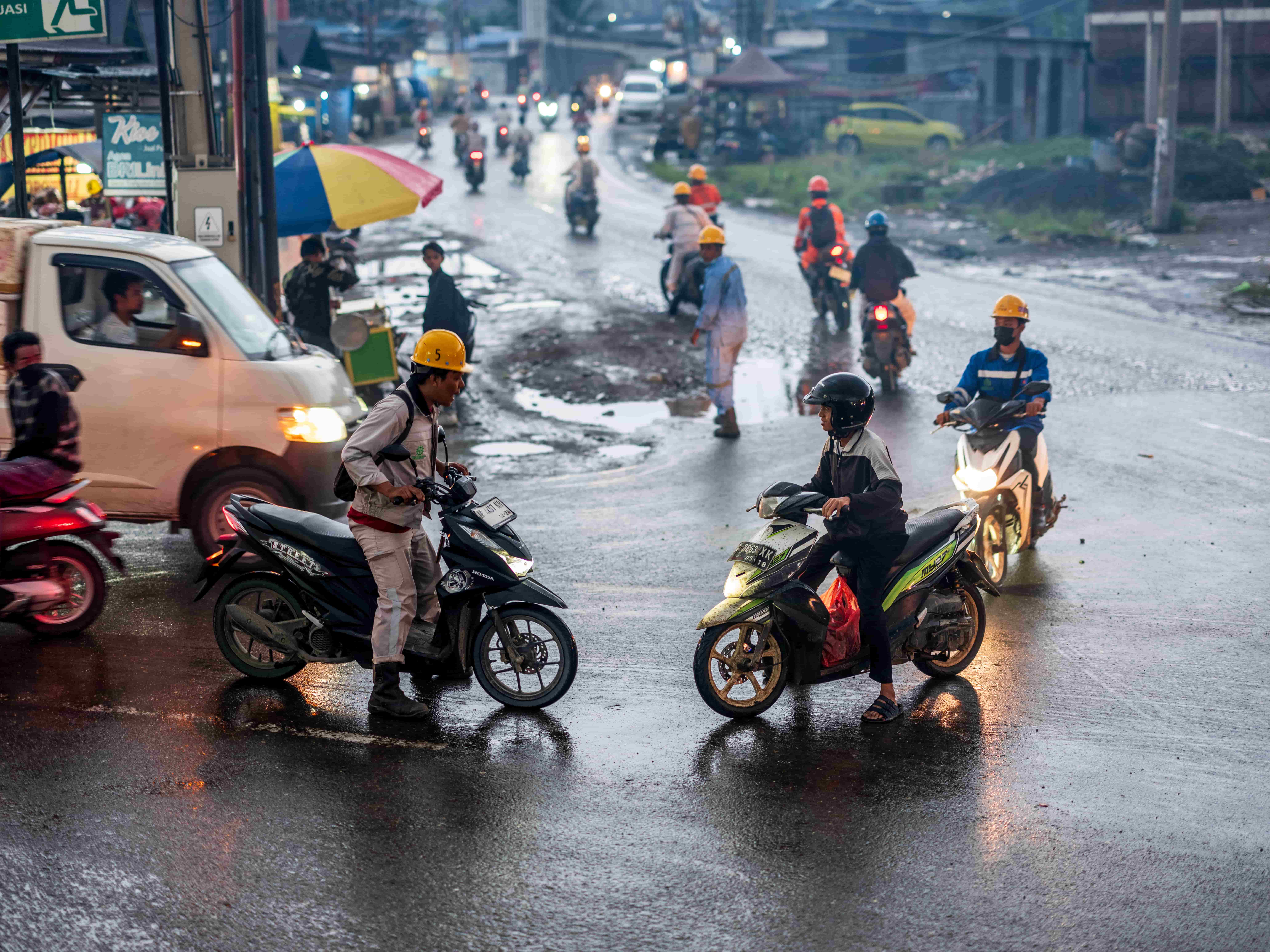 A mining worker on a moped stops and yells at another moped driving stopped directly in front of him on a wet road.