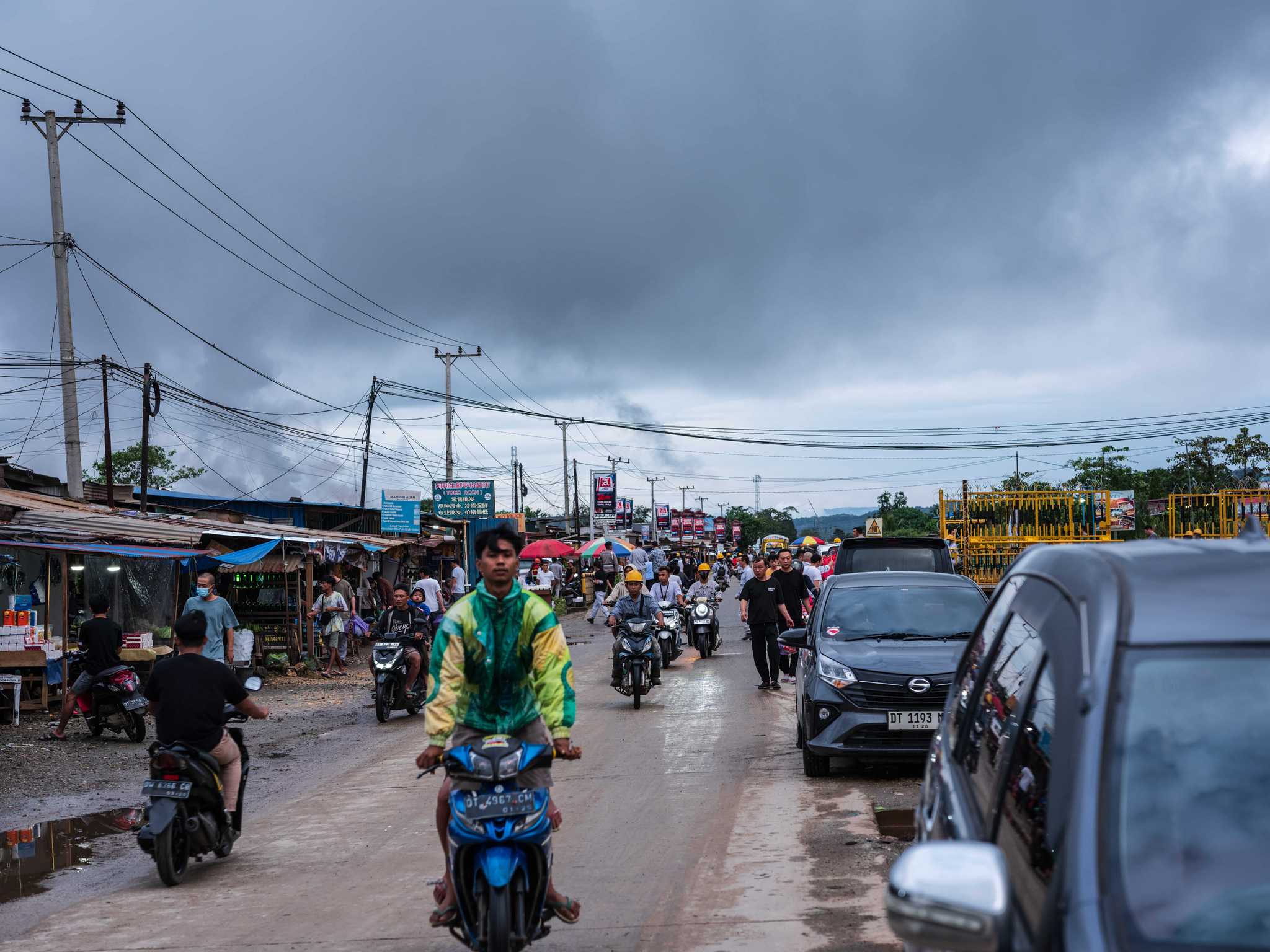 A rider in a bright jacket stands up on his moped as he drives through traffic with miners riding on mopeds behind him.