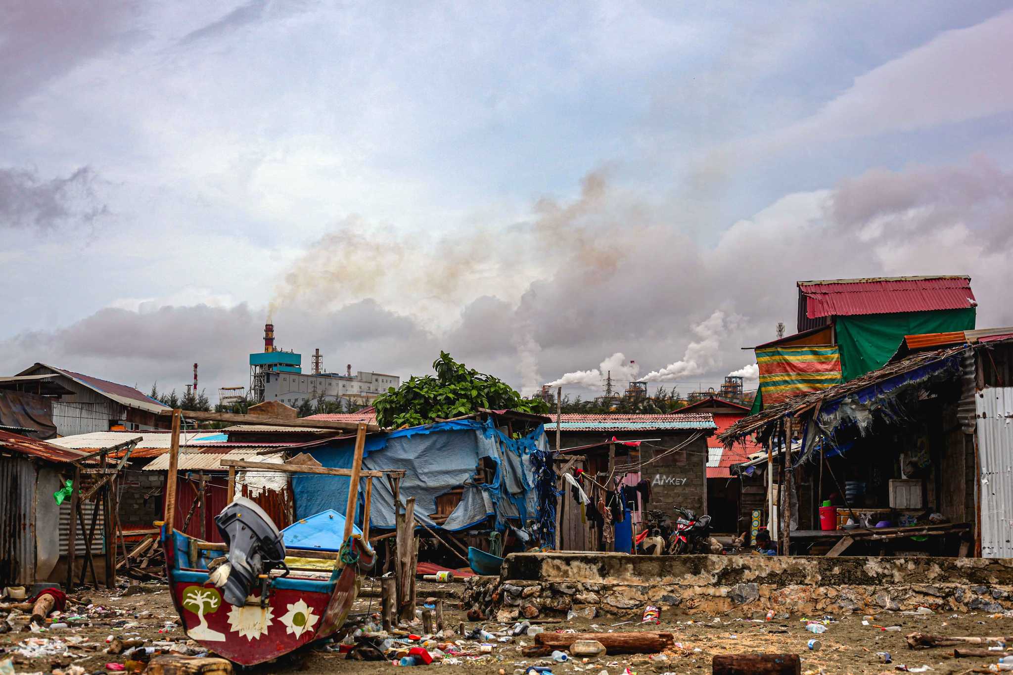 A boat in front of run down coastal shanty homes with trash covering the ground