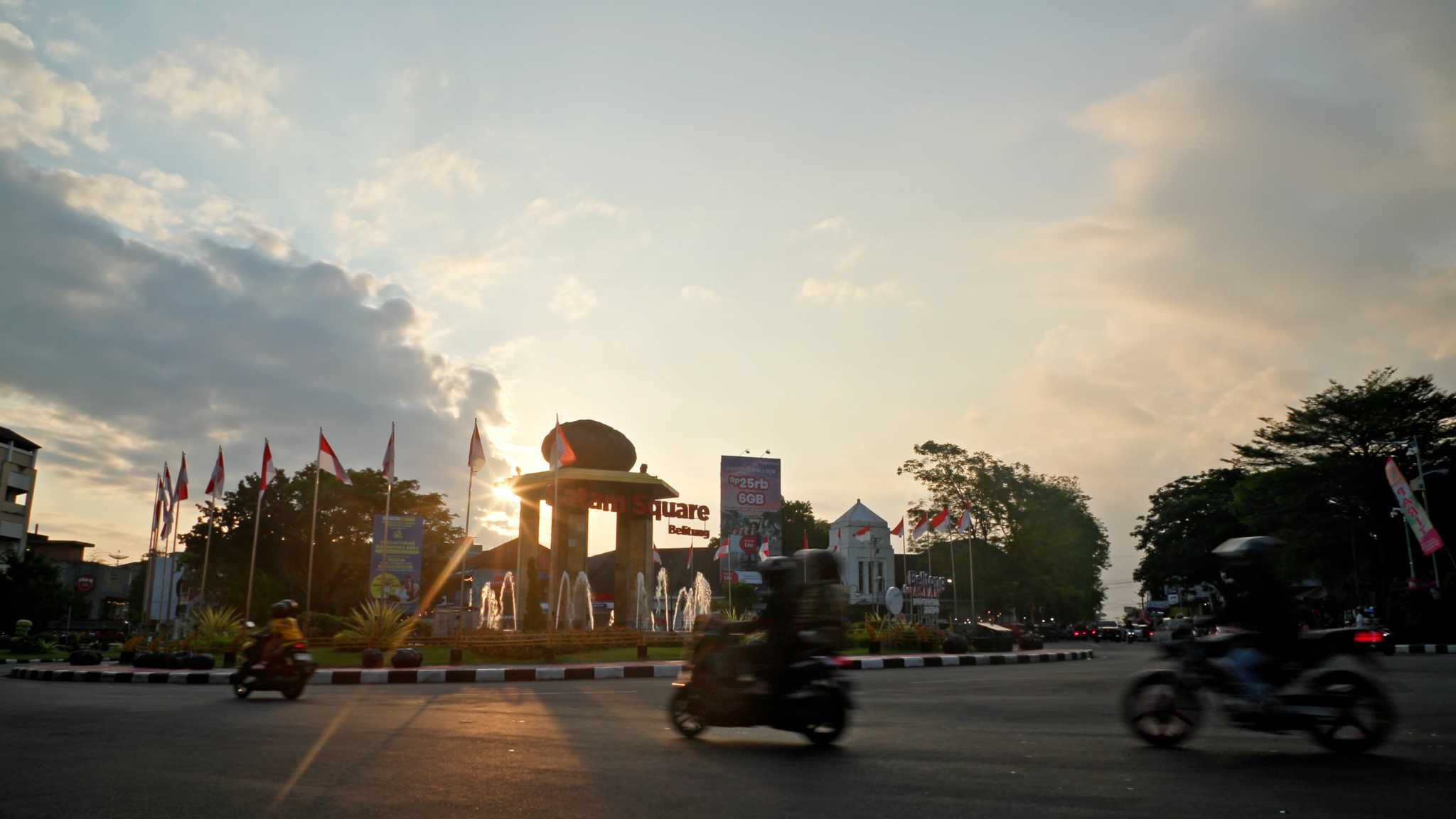 Scooters circle a busy road roundabout at sunset