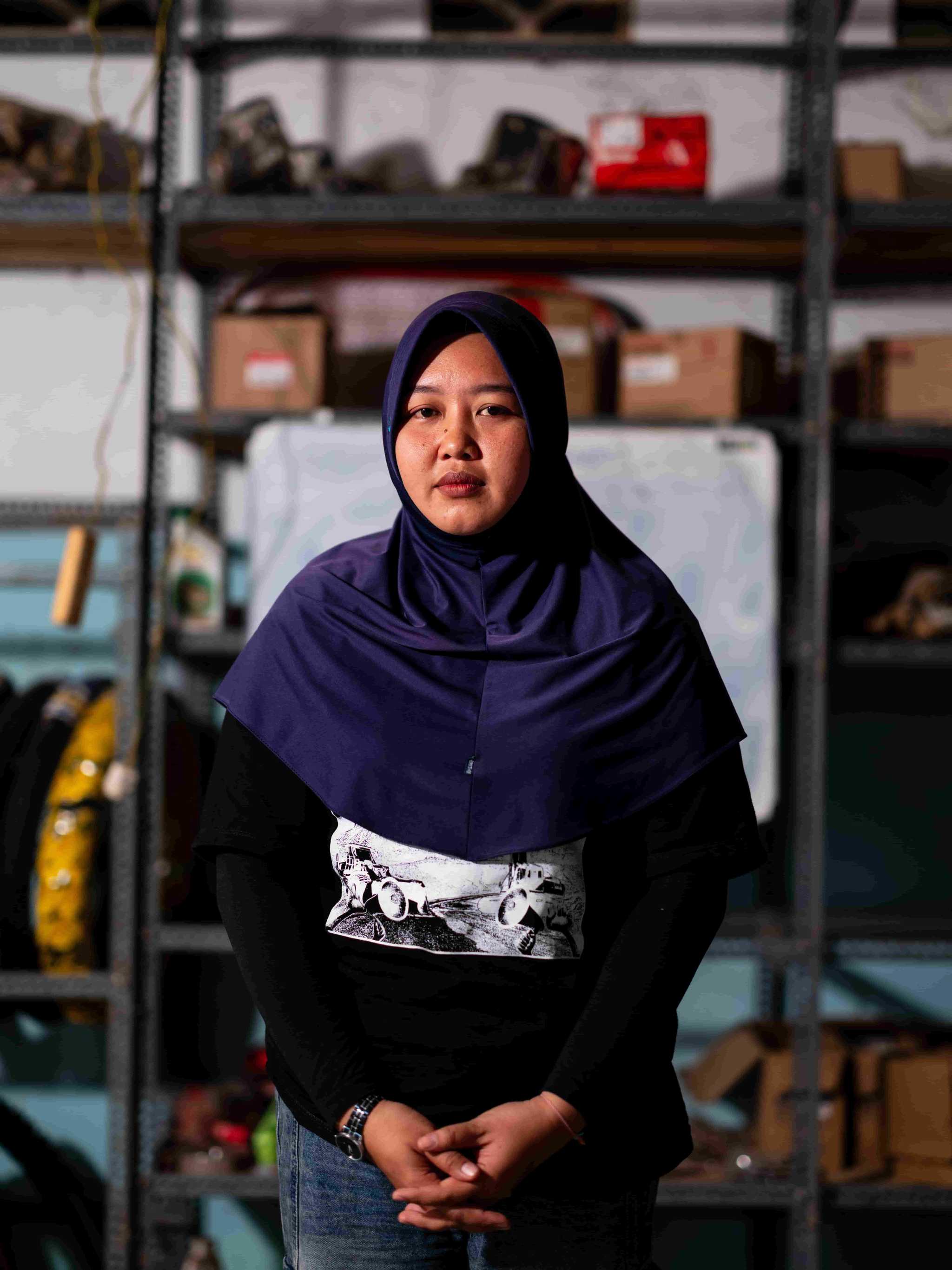 A young woman in a dark purple headscarf poses for a portrait in a garage.