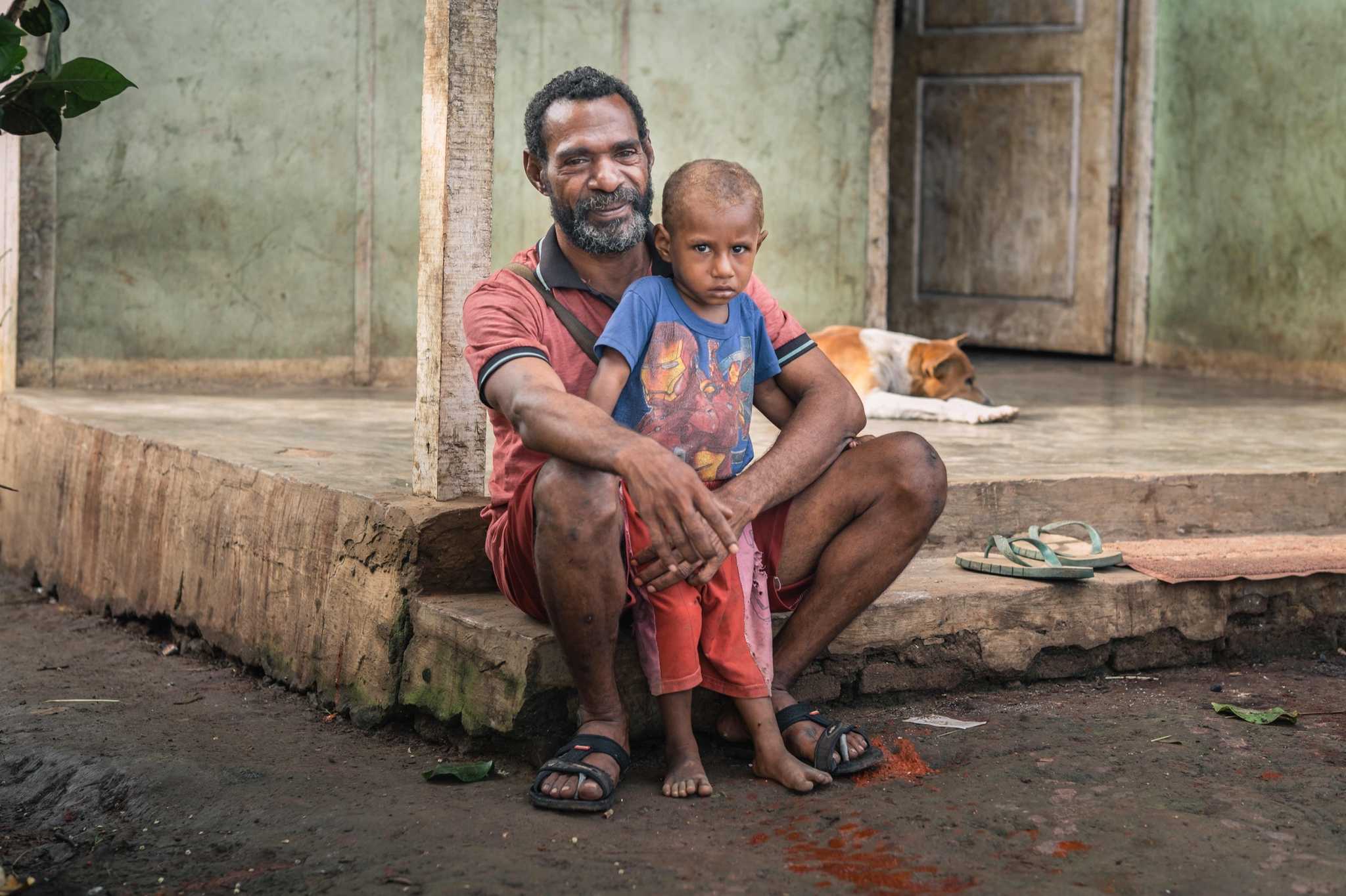 Natalis Basik-basik, the village head, sits with one of his children in front of their house in Zanegi.