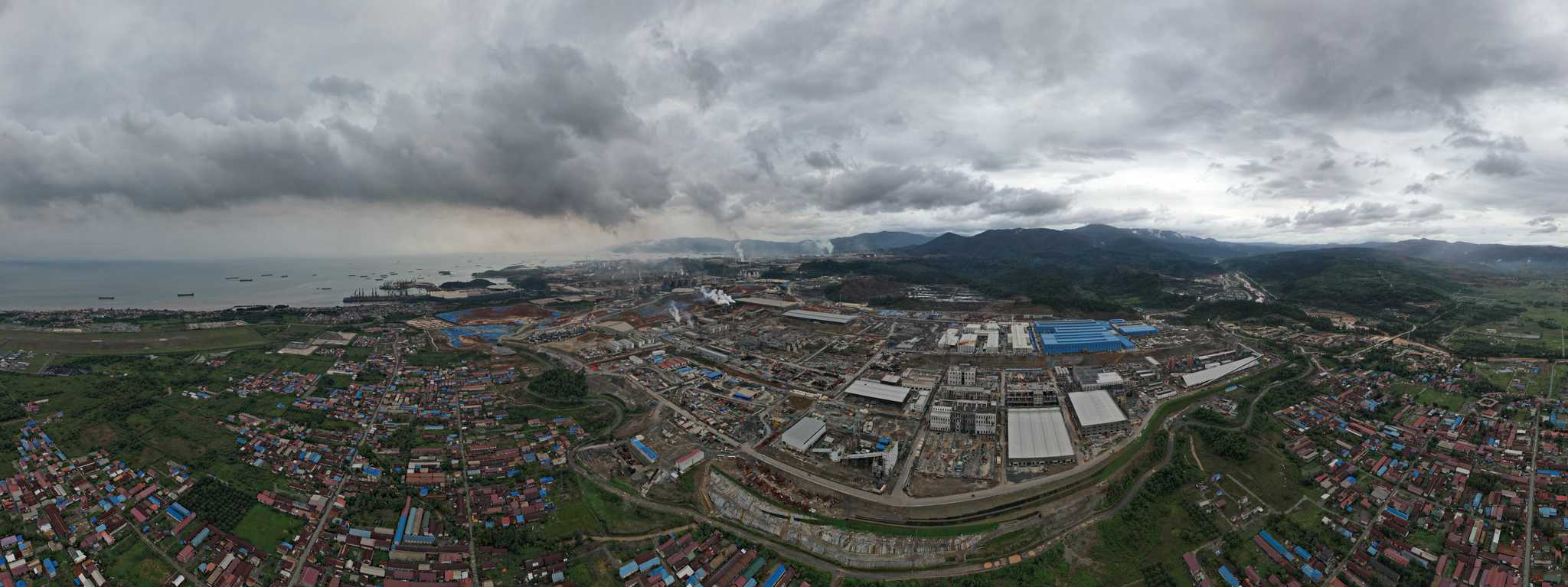 A panorama image of a large industrial mining park with settlements surrounding the facility and the sea in the distance.