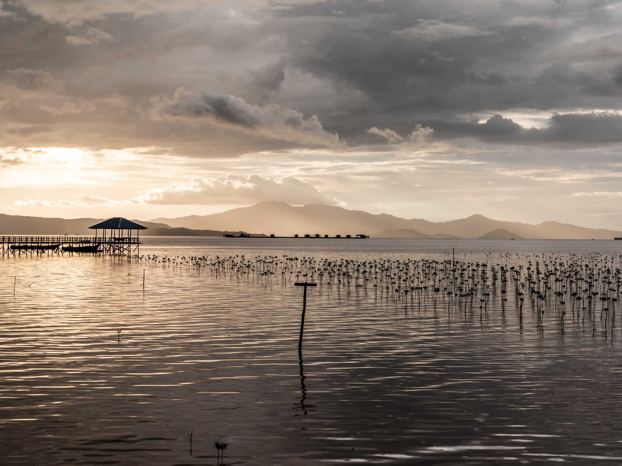 A sweeping shot of peaceful water with the sun setting behind clouds and mountains in the distance.