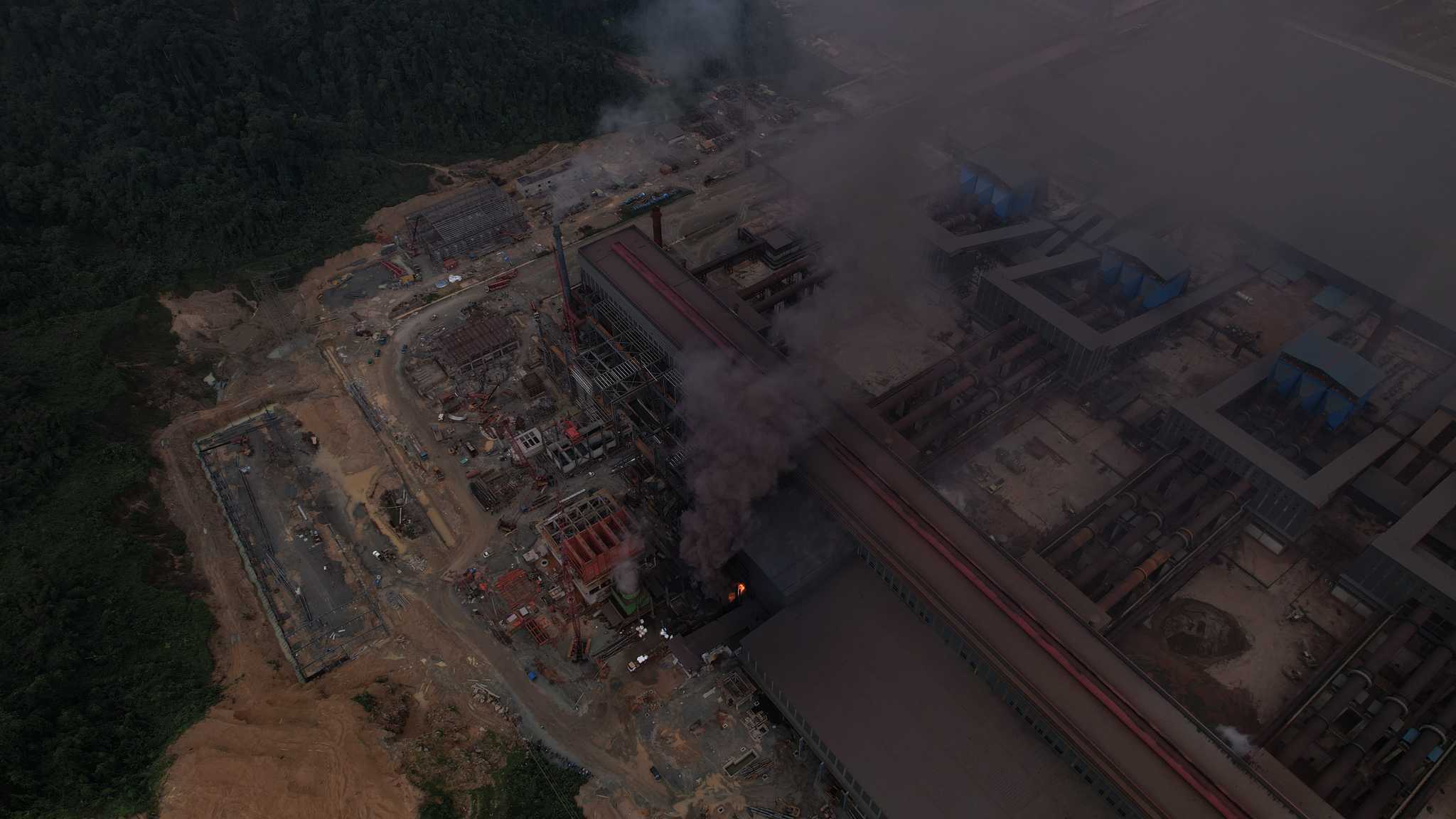 An aerial view of a smelting facility with a fire inside the building releasing dark black smoke.